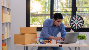 Küçük bir iş kurun, bağımsız KME girişimcisi, erkek, dizüstü bilgisayarlı ve sarı kutulu, genç Asyalı ofis sahibi, çevrimiçi pazarlama kutusu paketleme. eTicari dağıtım tele pazarlama satış fikirleri