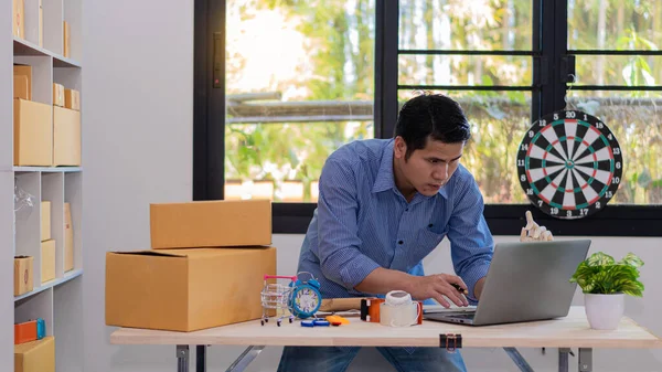 Küçük bir iş kurun, bağımsız KME girişimcisi, erkek, dizüstü bilgisayarlı ve sarı kutulu, genç Asyalı ofis sahibi, çevrimiçi pazarlama kutusu paketleme. eTicari dağıtım tele pazarlama satış fikirleri