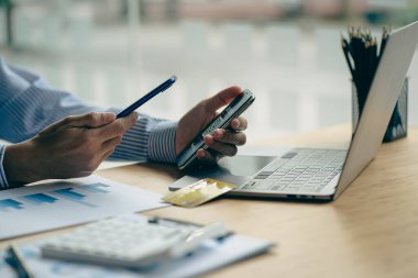 Akıllı telefonu tutan bir iş adamı, cihazlar üzerinde proje istatistikleri üzerinde çalışıyor. Grafikler ve girişimcinin bilgisayarının sunumu mali verileri analiz eder. Piyasadaki değişiklikleri göster