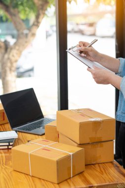 Küçük bir işletmenin portresi, sahibi, Asyalı girişimci kutular ve dizüstü bilgisayarlar üzerinde çalışıyor, kutuları hazırlamak için online siparişleri kontrol ediyor. Müşterilere satış, KOBİ iş konsepti, çevrimiçi satış adı