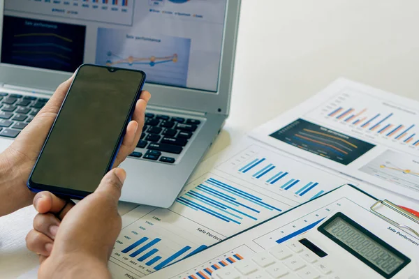 Akıllı telefonu tutan bir iş adamı, cihazlar üzerinde proje istatistikleri üzerinde çalışıyor. Grafikler ve girişimcinin bilgisayarının sunumu mali verileri analiz eder. Piyasadaki değişiklikleri göster