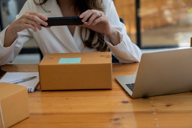Çevrimiçi satış yapan ve cep telefonu ve laptop kullanan genç bir kadın, küçük bir işletme kuruyor, posta kutusu, ambalaj, çevrimiçi pazarlama ve teslimat ile serbest Asyalı KOBİ girişimcisi.
