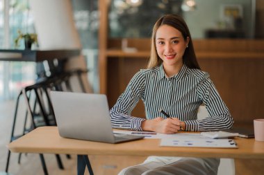 Modern ofiste dizüstü bilgisayar ve grafik döküman hesap makinesi üzerinde çalışan Asyalı iş kadını mali rapor analizi planlıyor. iş planı yatırımı başarılı