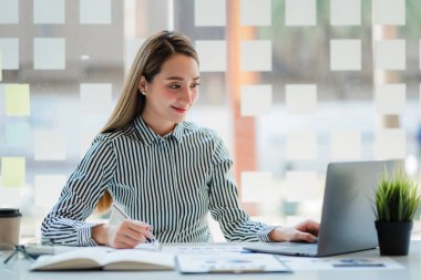 Modern ofiste dizüstü bilgisayar ve grafik döküman hesap makinesi üzerinde çalışan Asyalı iş kadını mali rapor analizi planlıyor. iş planı yatırımı başarılı