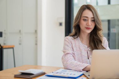 Modern ofiste dizüstü bilgisayar ve grafik döküman hesap makinesi üzerinde çalışan Asyalı iş kadını mali rapor analizi planlıyor. iş planı yatırımı başarılı