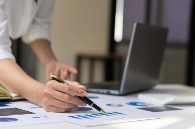 Kalemi grafiğe, mali verilere, araştırmaya, geliştirmeye ve piyasa raporuna işaret eden bir iş adamı. Ofiste bir hesap makinesi ve dizüstü bilgisayarla stratejik planlama, analiz ve hesaplama..