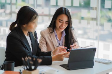 İki genç Asyalı iş kadınının iş birliği ve finans alanında başarılı olmak için bir takım olarak çalışması. Belgeler, grafikler ve tablet içeren selamlama ve fikirler.