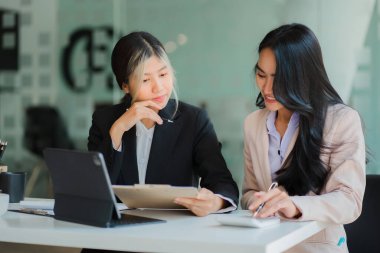 İki genç Asyalı iş kadınının iş birliği ve finans alanında başarılı olmak için bir takım olarak çalışması. Belgeler, grafikler ve tablet içeren selamlama ve fikirler.