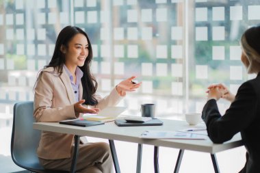 İki genç Asyalı iş kadınının iş birliği ve finans alanında başarılı olmak için bir takım olarak çalışması. Belgeler, grafikler ve tablet içeren selamlama ve fikirler.
