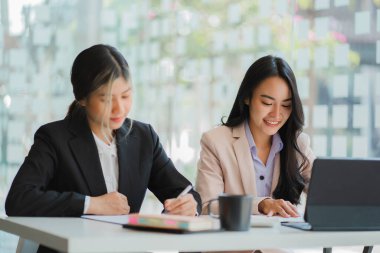 İki genç Asyalı iş kadınının iş birliği ve finans alanında başarılı olmak için bir takım olarak çalışması. Belgeler, grafikler ve tablet içeren selamlama ve fikirler.
