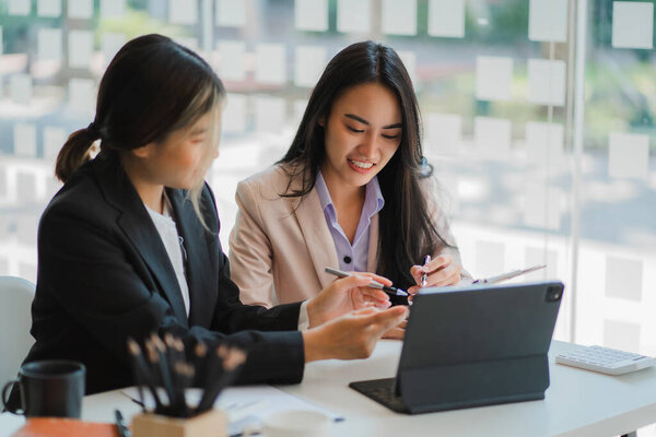 A meeting of two young Asian businesswomen to collaborate and work as a team for success in business and finance. Affiliate greetings and ideas with documents, graphs and a tablet on the table.