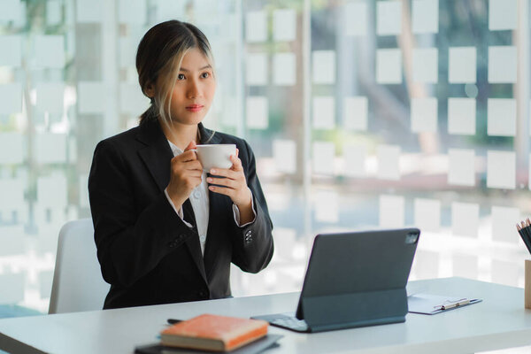 Asian businesswoman working with digital tablet, professional woman in a black business suit in office building representing a business idea.