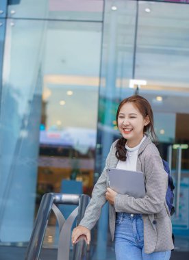 Alışveriş merkezinin önünde elinde tabletle duran Asyalı bir kız öğrenci ve evin dışında internet üzerinden çalışma fikri..