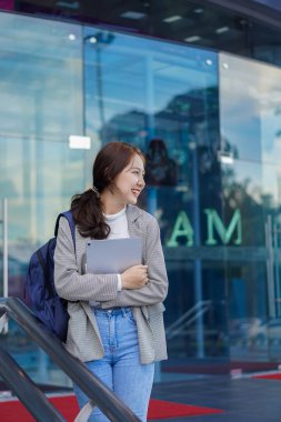 Alışveriş merkezinin önünde elinde tabletle duran Asyalı bir kız öğrenci ve evin dışında internet üzerinden çalışma fikri..
