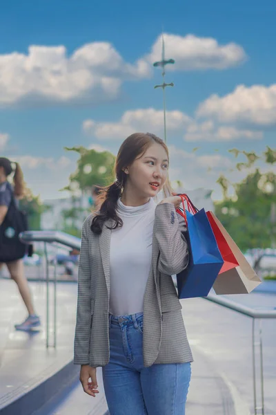 一位亚洲女人 提着一个五颜六色的购物袋 在购物中心前快乐地微笑着 — 图库照片