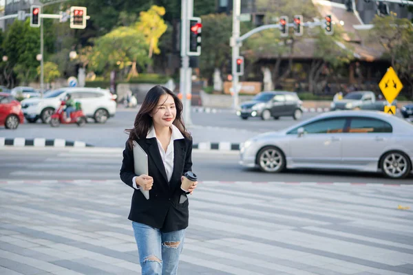 一位拿着笔记本电脑和咖啡杯的年轻亚洲女商人兴高采烈地走进办公室 — 图库照片