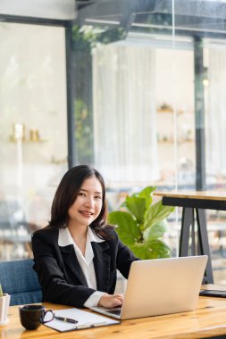 Bilgisayarlı ekran ekranına bakan Asyalı kadın kahve dükkanında çalışma konseptine bakarak telekomünikasyon yaparken e-posta ya da araştırma yapıyor.