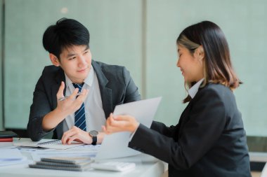 İki genç Asyalı iş adamı konferans odasında başarılı bir modern ofis kurma konusunda fikir alışverişinde bulunuyor..