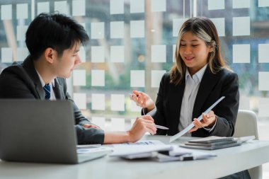 İki genç Asyalı iş adamı konferans odasında başarılı bir modern ofis kurma konusunda fikir alışverişinde bulunuyor..
