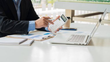 Şirket hesaplarından gelen rakamları hesaplamak ve yıllık mali raporları hazırlamak için beyaz hesap makinesine basan bir finans işadamının yakın çekimi. Finansal numaraların doğrulanması