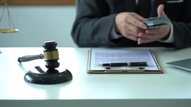 Asyalı erkek avukat, mahkeme masasında tahta çekiçle para sayıyor ve tanrıça terazisi adalet ve hukuk danışmanlığı kavramına sahip.