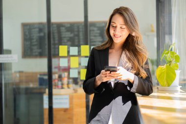 Asyalı iş kadınları ofisteki internet üzerinden mesaj göndermek için akıllı telefon kullanıyorlar.