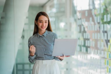 Başarılı Asyalı iş kadını masasının önünde dizüstü bilgisayar tutuyor..