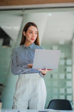Successful Asian businesswoman happily holding a laptop in front of her desk.
