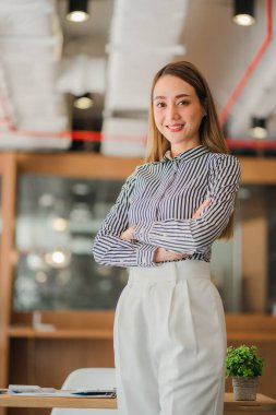 Başarılı ve kendinden emin Asyalı iş kadını masasının önünde mutlu bir şekilde oturuyor..