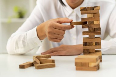 Ticarette alternatif riskler için kavramlar, planlar ve stratejiler. Bir ağaç bloğu işletmesinin riskleri. Bir işadamı bir bina oluşturmak için istiflenmiş bir kuleye tahta bloklar koyar ve çeker..