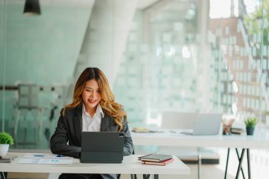 An Asian female accountant sits at a desk with a laptop and calculates financial graphs showing investment results. Plan a successful business growth process in the office.