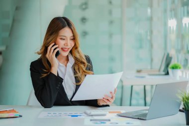 Asyalı bir kadın muhasebeci dizüstü bilgisayarla masada oturuyor ve yatırım sonuçlarını gösteren finansal grafikleri hesaplıyor. Ofiste başarılı bir iş büyüme süreci planlayın.