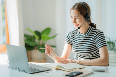 Dizüstü bilgisayar kullanarak kulaklık takan genç Asyalı öğrenci bir dil öğrenme hakkında bir not yaz. Webinarlar çevrimiçi görünsün. ses dinleme kursu e-öğrenme kavramı