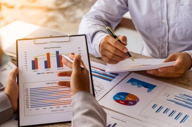 Kalemleri olan iki işadamının yakın plan fotoğrafları, dizüstü bilgisayarla ahşap masada sohbet ederken, takım çalışması, finansal hesapları ve piyasa ekonomisini tartışırken..