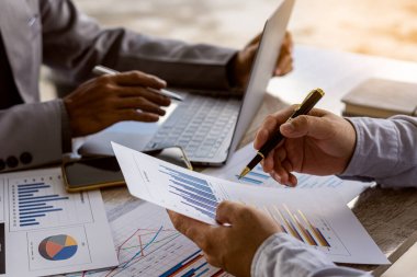 Kalemleri olan iki işadamının yakın plan fotoğrafları, dizüstü bilgisayarla ahşap masada sohbet ederken, takım çalışması, finansal hesapları ve piyasa ekonomisini tartışırken..