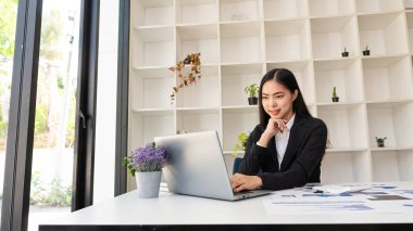 İş konularında finansal grafikleri analiz eden bir dizüstü bilgisayar üzerinde çalışan Asyalı işkadını, başlangıç projelerinin finansmanını tartışıyor