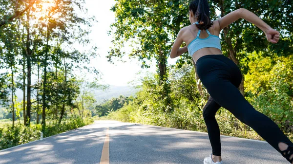 Spor kıyafetli ince bir kız aydınlık bir sabahta yolda koşuyor, sonbahar ormanında koşuyor. Arkadan bak. Yoldayım. Açık havada çekim..