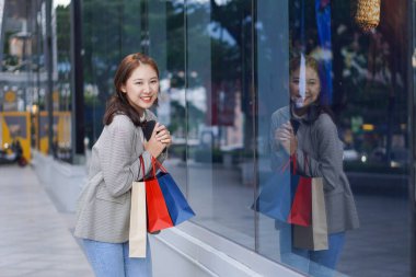 Çanta tutan Asyalı kız alışveriş merkezinde alışveriş yaparken akıllı telefonunu kullan. Alışveriş merkezinin önündeki festivalde alışveriş yaptıktan sonra bolca alışveriş yapan güzel bir kızın portresi..
