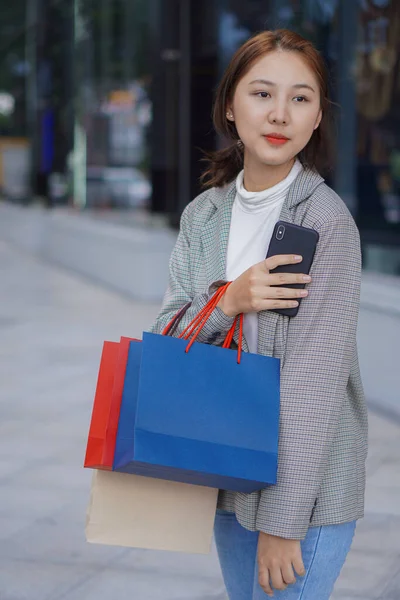 亚洲女孩提着一个包在商场购物时使用你的智能手机 一个漂亮的女孩在商场前购物后尽情享受购物的肖像 — 图库照片
