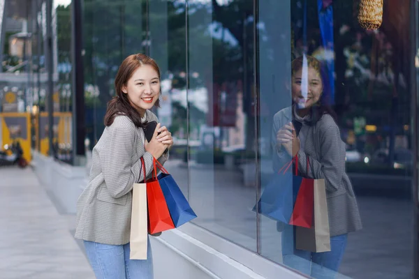 Çanta tutan Asyalı kız alışveriş merkezinde alışveriş yaparken akıllı telefonunu kullan. Alışveriş merkezinin önündeki festivalde alışveriş yaptıktan sonra bolca alışveriş yapan güzel bir kızın portresi..