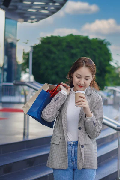 Çanta tutan Asyalı kız alışveriş merkezinde alışveriş yaparken akıllı telefonunu kullan. Alışveriş merkezinin önündeki festivalde alışveriş yaptıktan sonra bolca alışveriş yapan güzel bir kızın portresi..