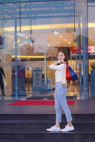 Çanta tutan Asyalı kız alışveriş merkezinde alışveriş yaparken akıllı telefonunu kullan. Alışveriş merkezinin önündeki festivalde alışveriş yaptıktan sonra bolca alışveriş yapan güzel bir kızın portresi..