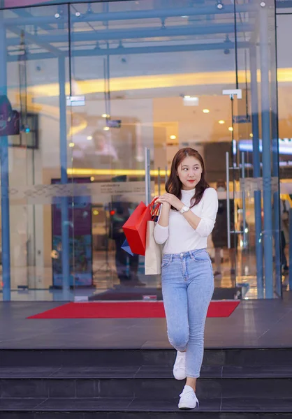 Çanta tutan Asyalı kız alışveriş merkezinde alışveriş yaparken akıllı telefonunu kullan. Alışveriş merkezinin önündeki festivalde alışveriş yaptıktan sonra bolca alışveriş yapan güzel bir kızın portresi..