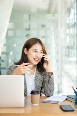 Asyalı bir kadın, serbest meslek sahibi, dizüstü bilgisayarla cep telefonuna odaklanmış. Finansal analiz, grafikler, hesaplar, grafikler, çevrimiçi pazarlama planları, ev dışındaki kahve dükkanlarına dayalı çalışma kavramları.