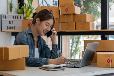 Girişimci, küçük işletme, KOBİ, yanında bir sürü kutuyla evden çalışan serbest çalışan kadın. Ticari izleme için akıllı telefonlar ve dizüstü bilgisayarlar kullanın. çevrimiçi pazarlama paketleme kutusu çevrimiçi satışları