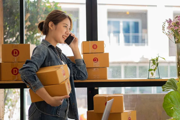 Girişimci, küçük işletme, KOBİ, yanında bir sürü kutuyla evden çalışan serbest çalışan kadın. Ticari izleme için akıllı telefonlar ve dizüstü bilgisayarlar kullanın. çevrimiçi pazarlama paketleme kutusu çevrimiçi satışları