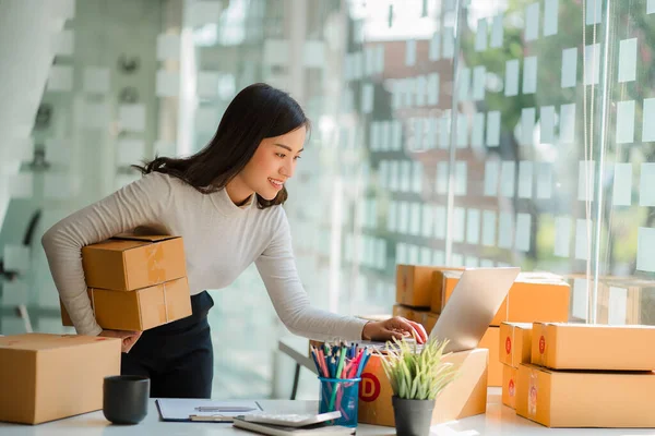 Küçük bir iş kurun, bağımsız KME girişimcisi, evden, kutudan, akıllı telefondan, bilgisayardan, çevrimiçi, pazarlamadan, paketlemeden, nakliyattan, parsel KME 'den, eCommerce konseptinden çalışan Asyalı kadının portresi.