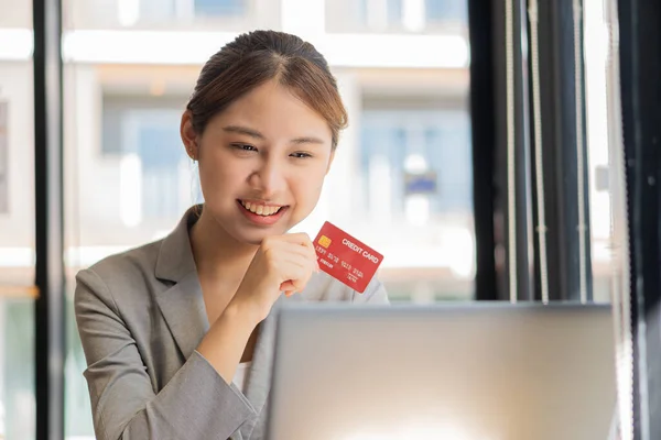 Young Asian businesswoman using credit card and for financial payments and online shopping on laptops, retail stores, e-commerce, smartphones, smart payment transactions, money transfer technology.