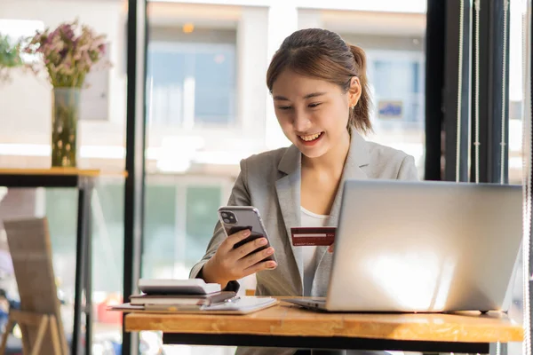 Kredi kartı kullanan genç Asyalı iş kadını ve finansal ödemeler ve dizüstü bilgisayarlarda online alışveriş, perakende mağazaları, e-ticaret, akıllı telefonlar, akıllı ödeme işlemleri, para transfer teknolojisi.