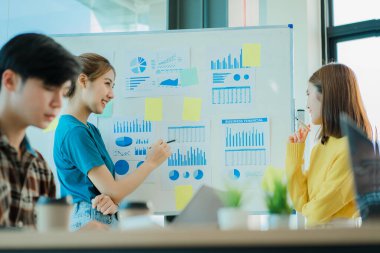 Bir grup Asyalı genç iş adamı yeni nesil yaratıcı genç dizüstü bilgisayarlara beyin fırtınası yapıyor. Toplantıda yeni başlatılan projeler için fikir alışverişinde bulunun ve tartışın.